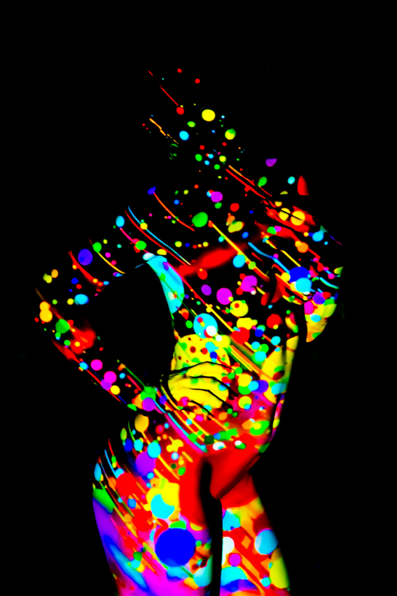 Nude figure covered in bright multicolored patterns against a black background.