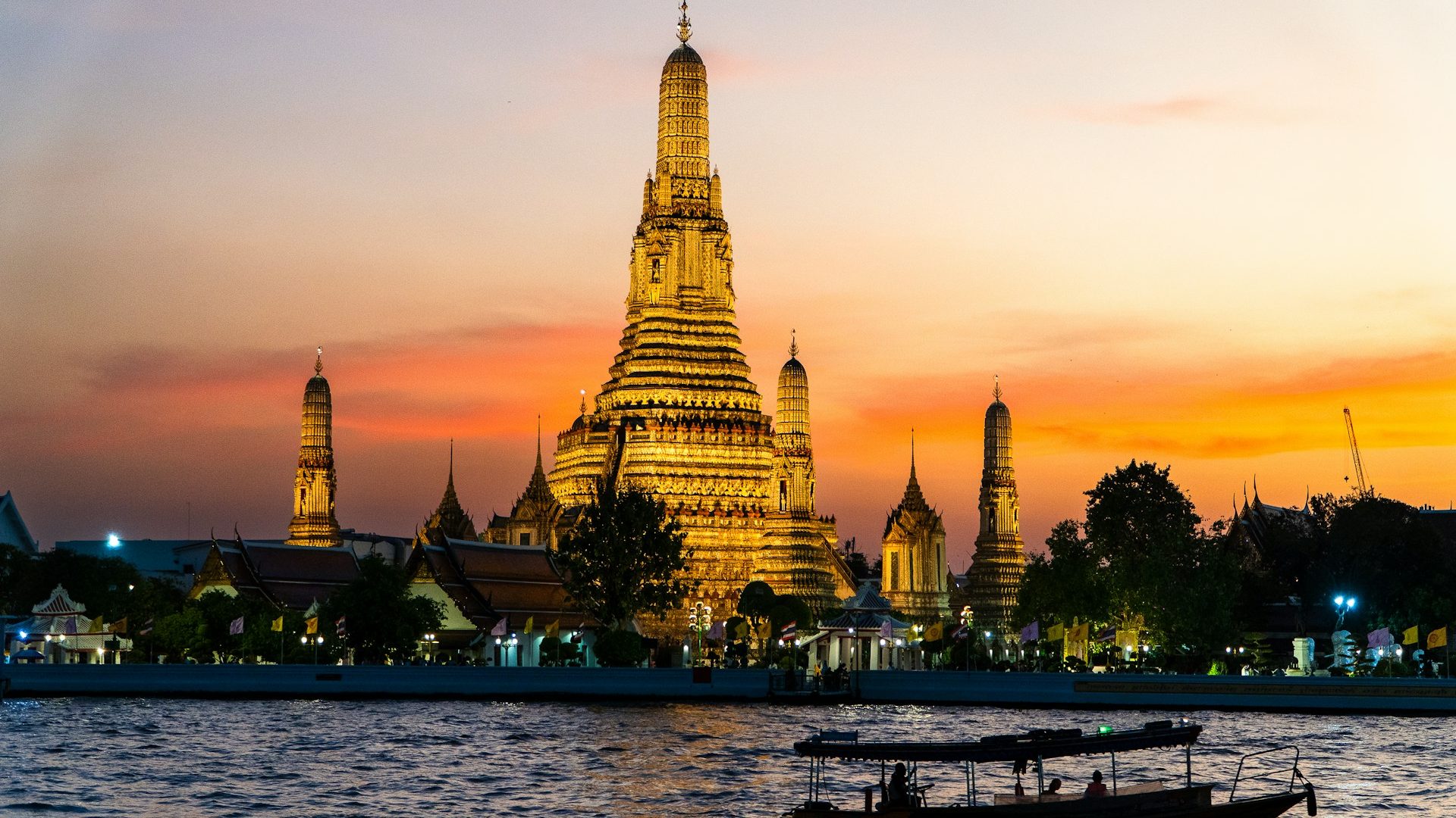 The illuminated Wat Arun temple at sunset with a boat on the river in the foreground