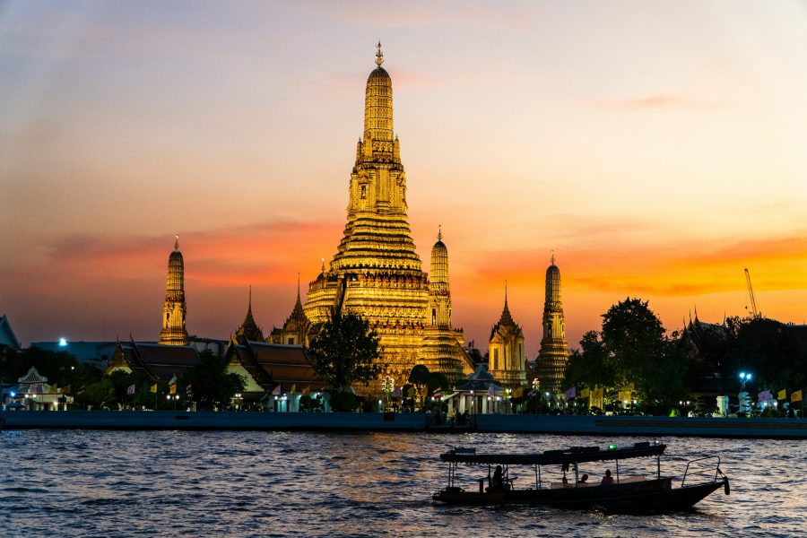 The illuminated Wat Arun temple at sunset with a boat on the river in the foreground