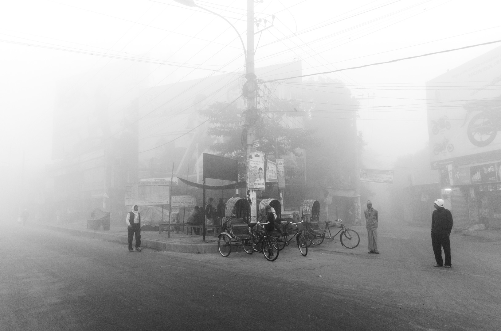 Foggy city street with people, bicycles and a tall utility pole.