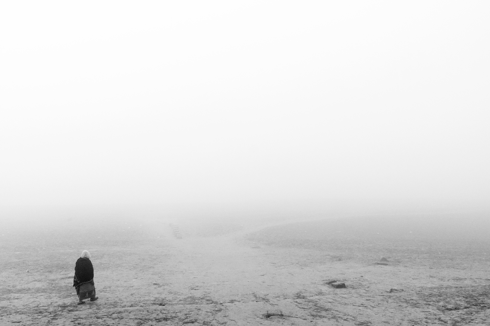 A lone figure crossing an open field under heavy fog.