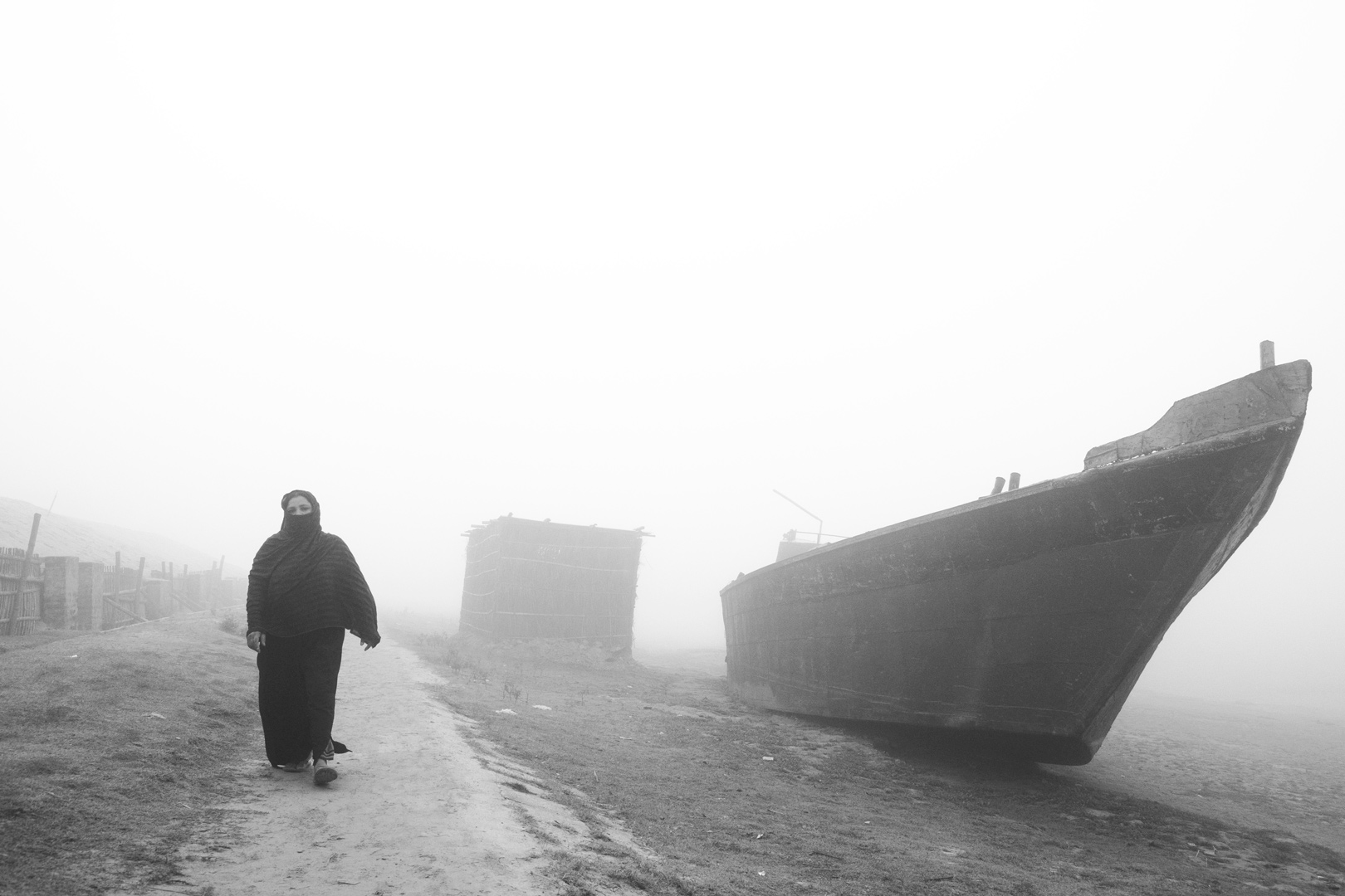 A person walks past a large beached boat in dense fog.