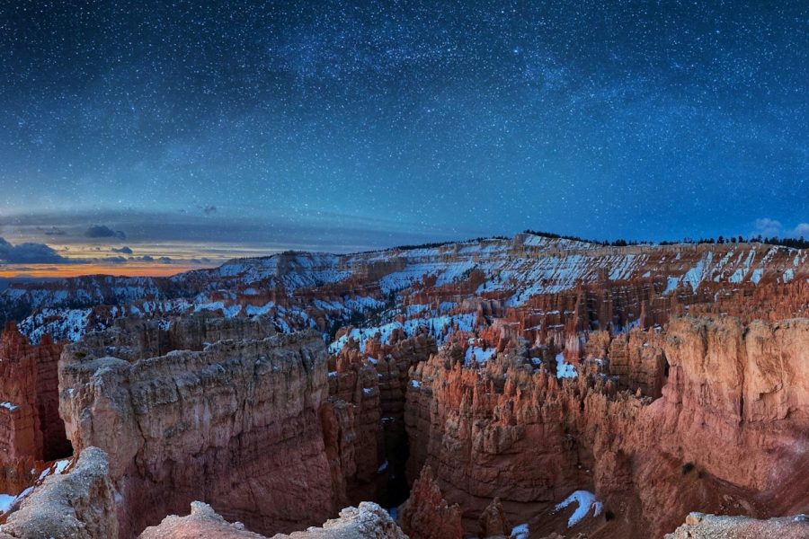 Snow-dusted red rock hoodoos of a canyon amphitheater under a starry night sky
