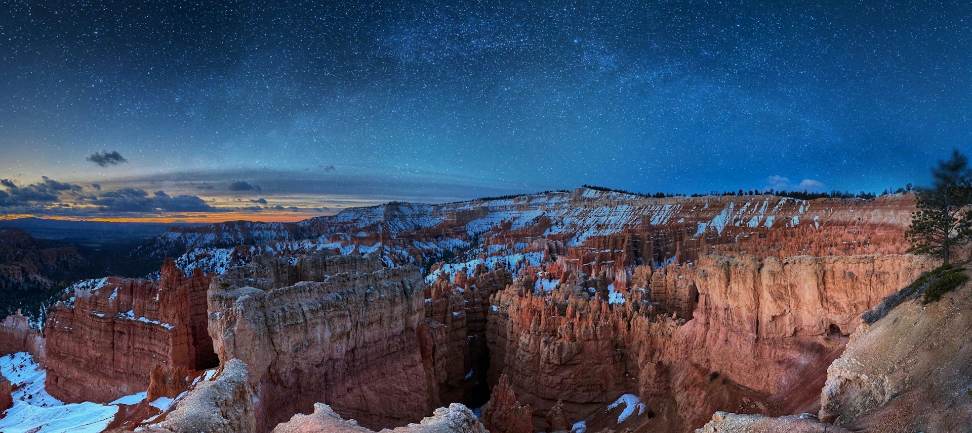Snow-dusted red rock hoodoos of a canyon amphitheater under a starry night sky