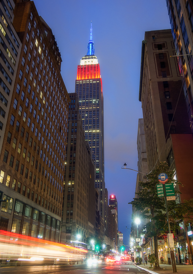 Empire State Building illuminated above a city street at dusk.
