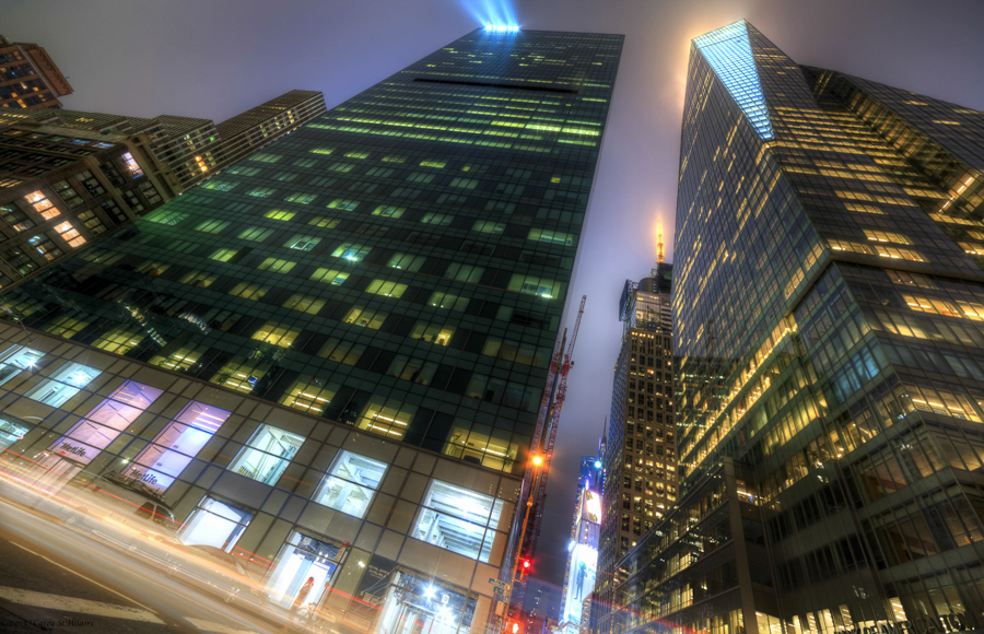 Upward night view between tall glass office buildings.