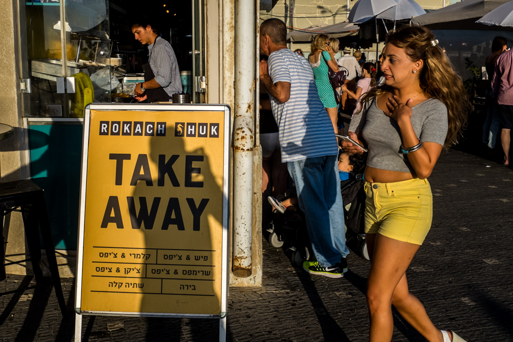 A woman in yellow shorts walks past a yellow take-away sign.