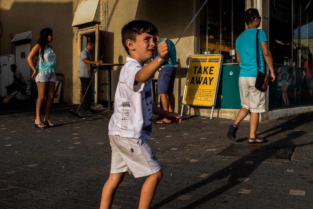 Boy drinks from a blue cup while walking past a take-away stand.