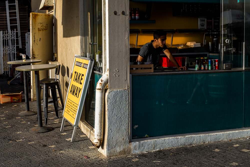 Worker behind the counter of a take-away restaurant, with a yellow sign outside.