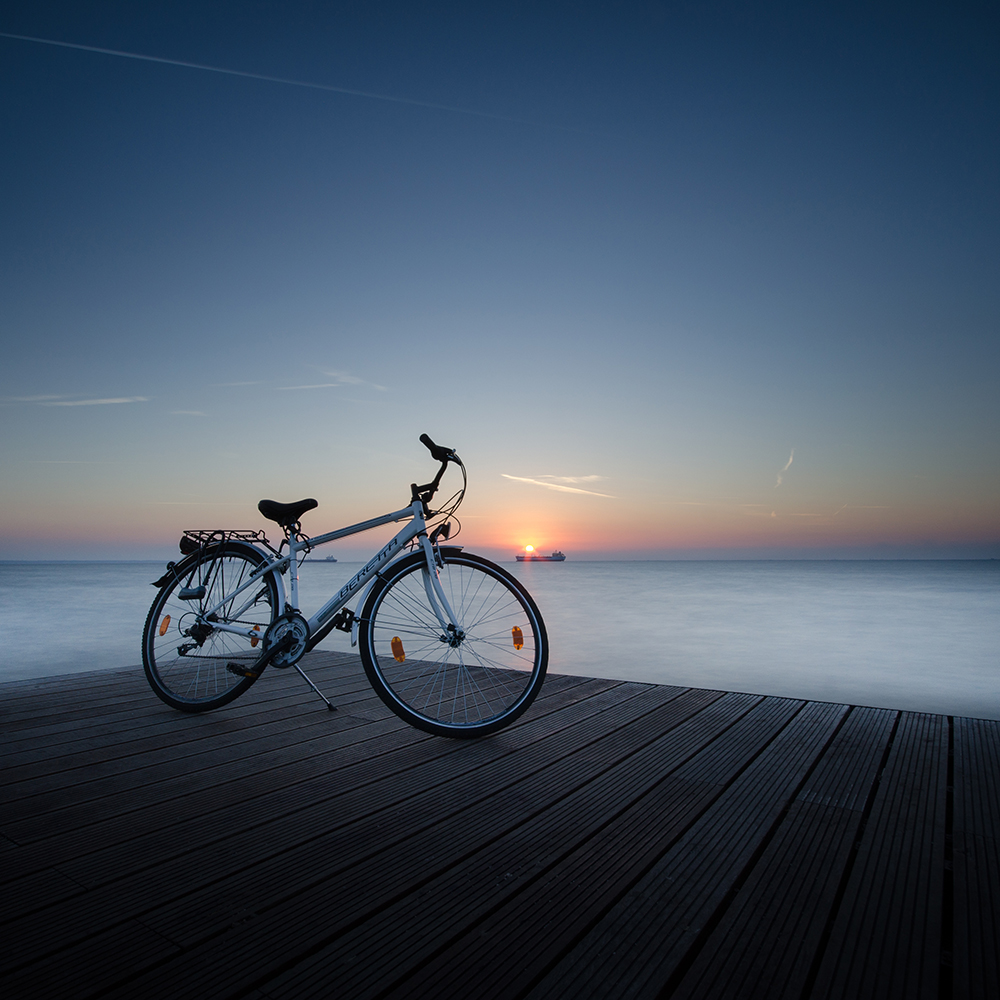 A bicycle stands on a wooden waterfront deck at sunset.