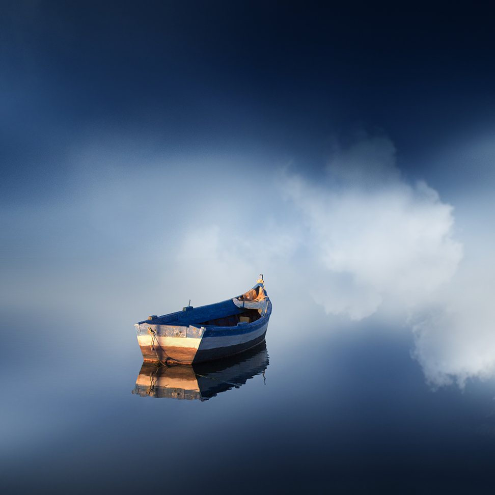 A small blue boat and its reflection sit against clouds in dark water.