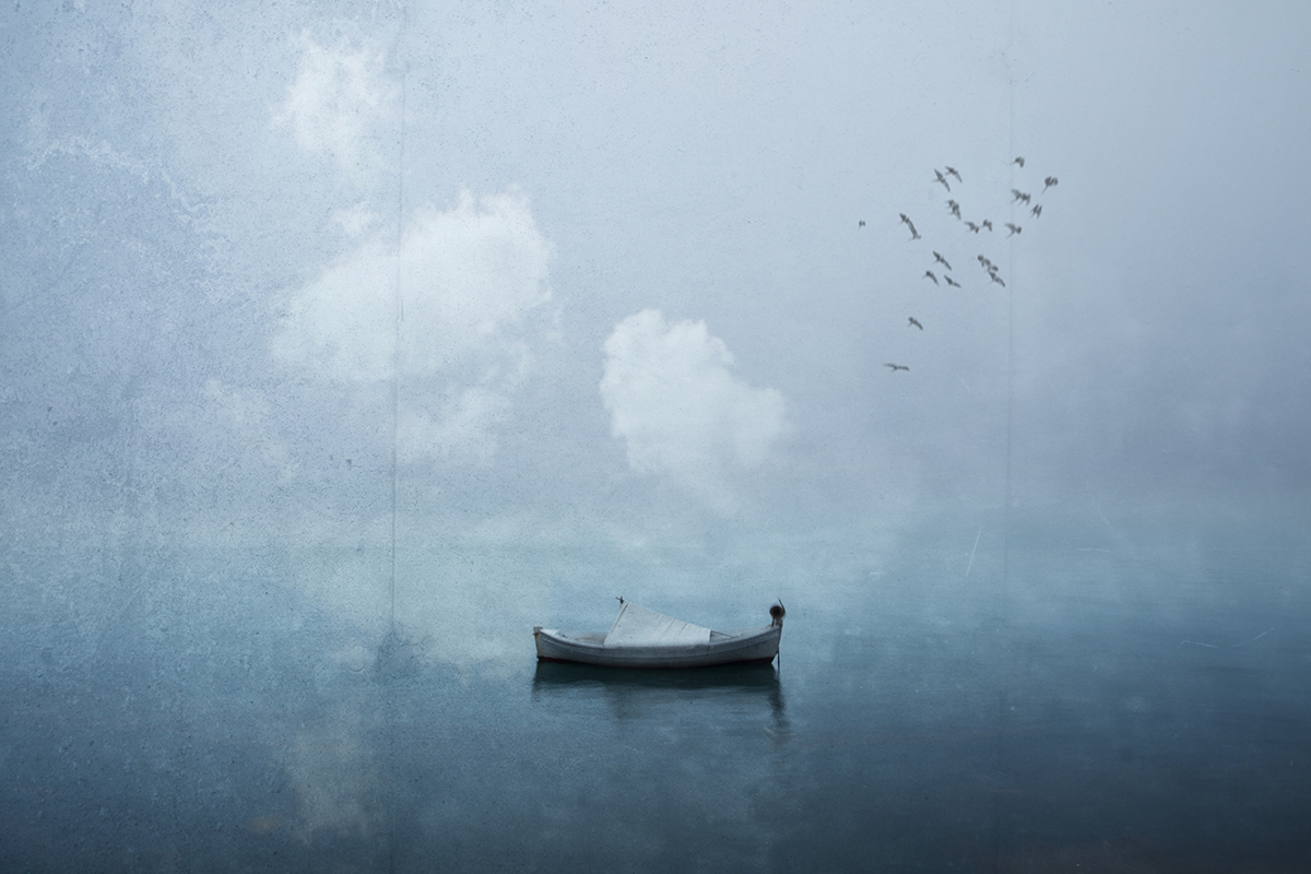 A small rowboat floats on still misty water beneath a flock of birds.