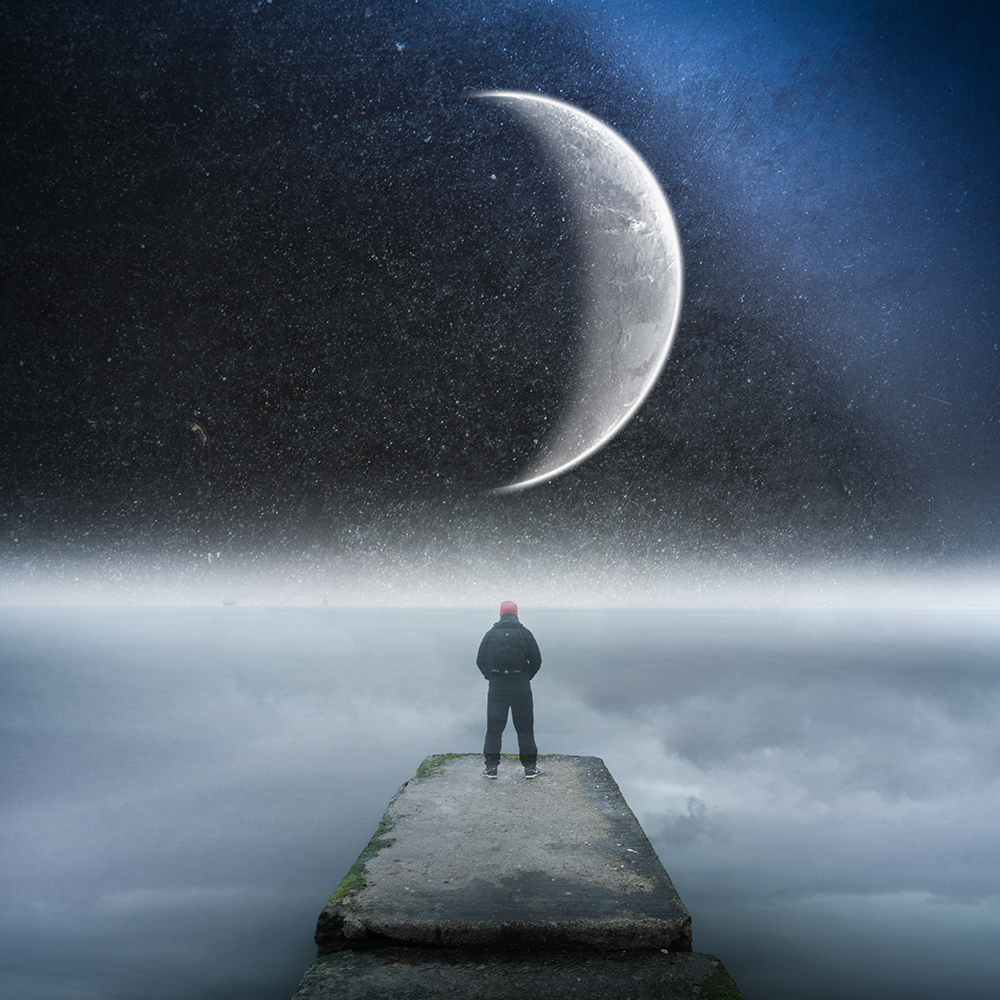 A person stands at the end of a concrete pier beneath an oversized crescent moon.