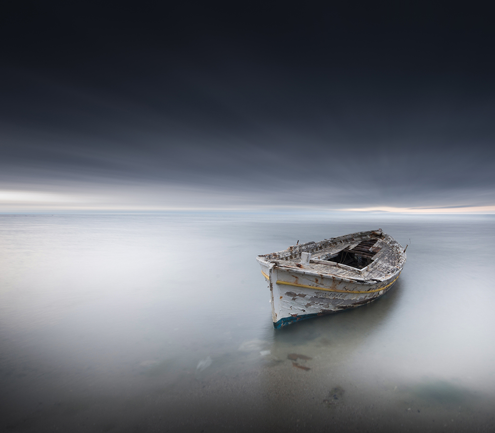 An old wooden boat rests in still shallow water under a dark sky.