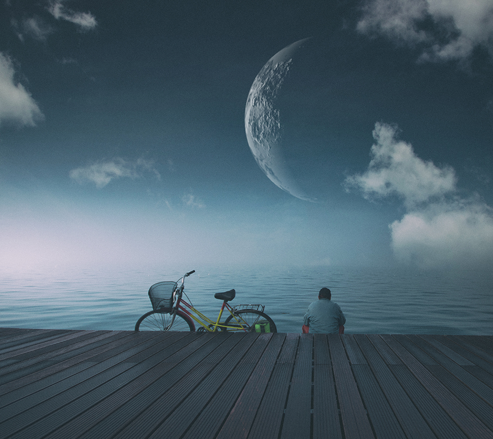 A person sits beside a bicycle on a pier beneath a large composited moon.