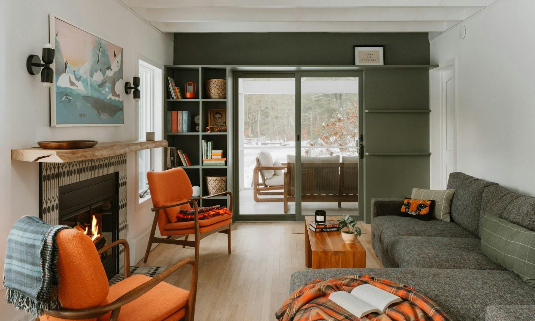 Warm living room with orange chairs, a lit fireplace, gray sofa, and patio doors.