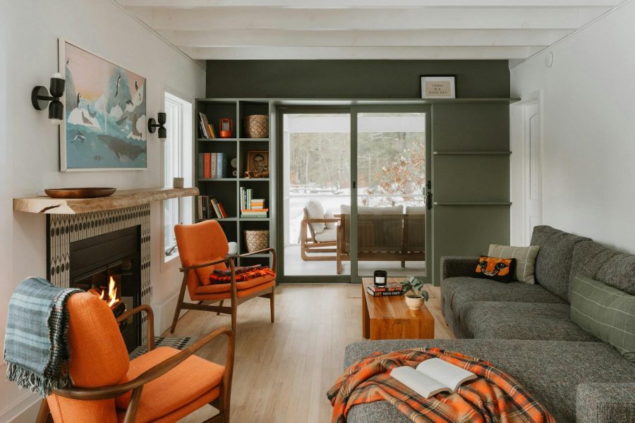 Warm living room with orange chairs, a lit fireplace, gray sofa, and patio doors.
