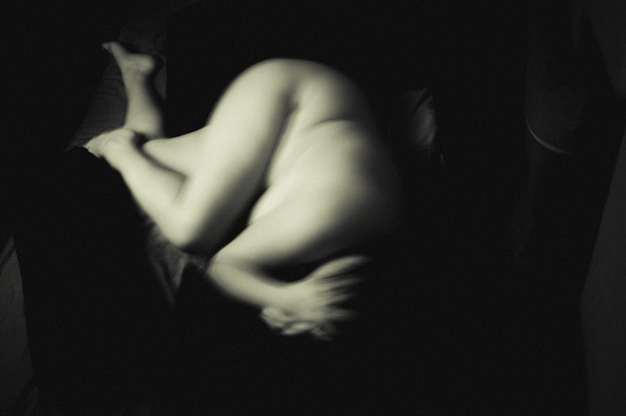 Blurred nude figure curled against a dark background.