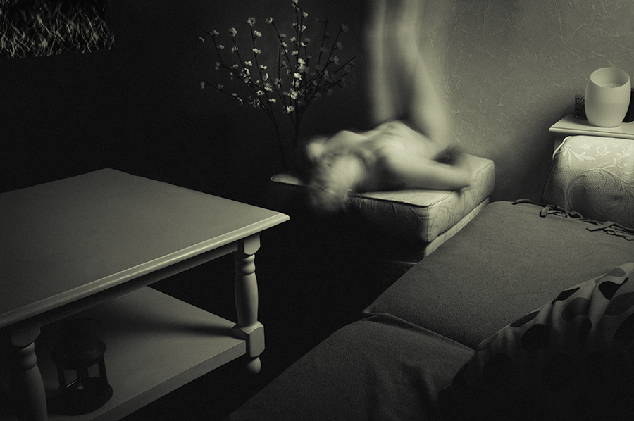 Blurred figure moving across an armchair in a room with a coffee table and sofa.