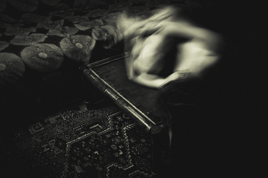 Blurred nude figure curled beside a low wooden table and patterned sofa.