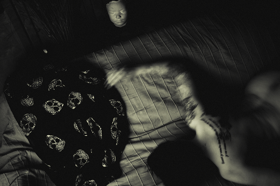 Overhead black-and-white view of a blurred figure beside a patterned rug and wooden floor.