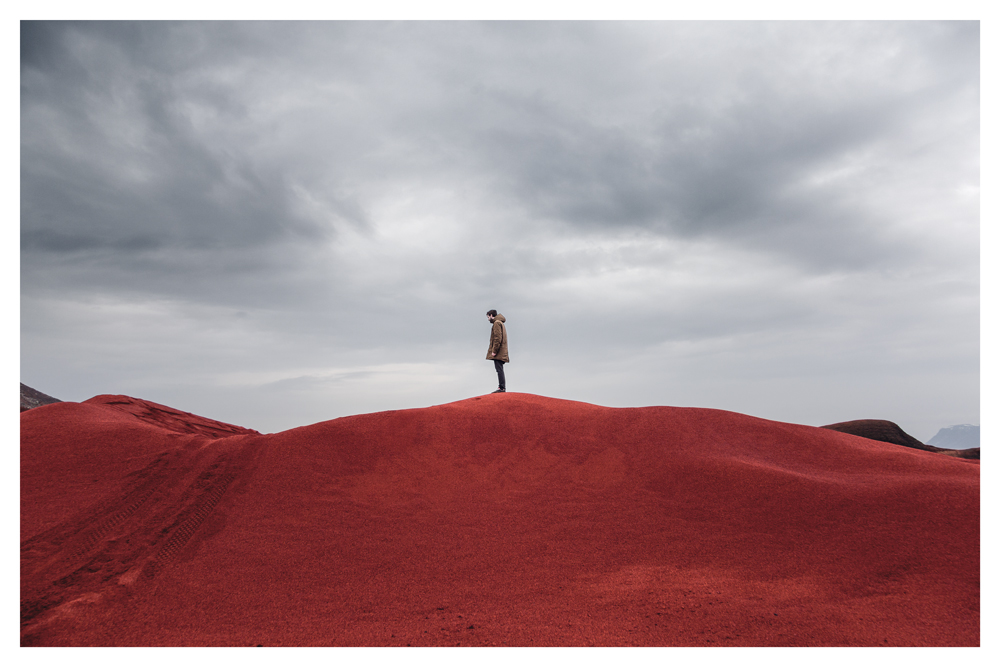 A person stands atop a red hill beneath an overcast sky - Pause by Juan Antonio Partal