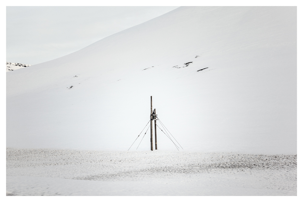 A pair of wooden poles and guy wires stands alone in a broad field of snow - Pause by Juan Antonio Partal