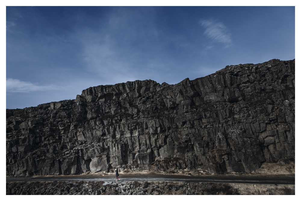 A person walks along the base of a towering dark rock cliff - Pause by Juan Antonio Partal