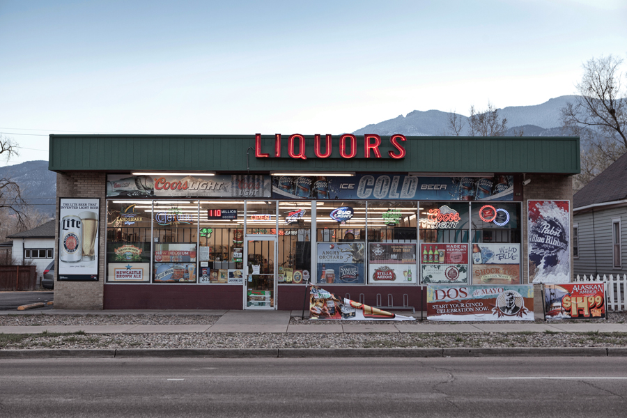 Liquor store storefront covered with posters and signs beneath a blue sky.