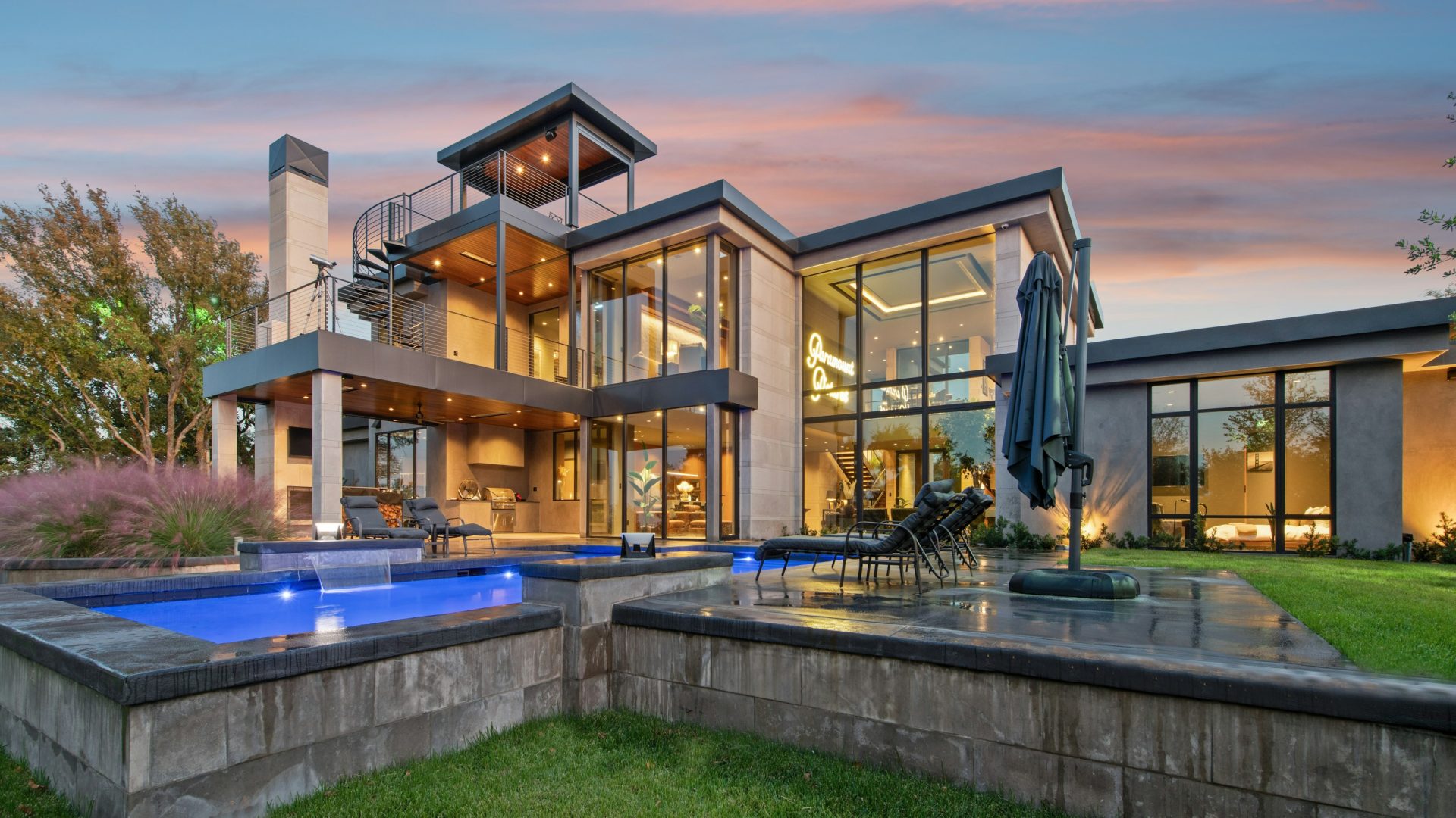 Modern home with lit windows and swimming pools at dusk