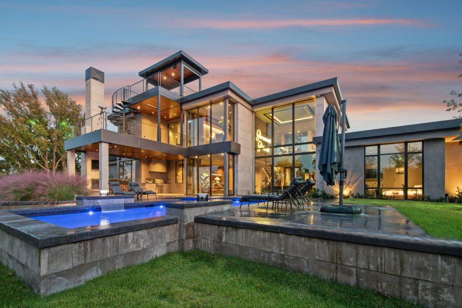 Modern home with lit windows and swimming pools at dusk