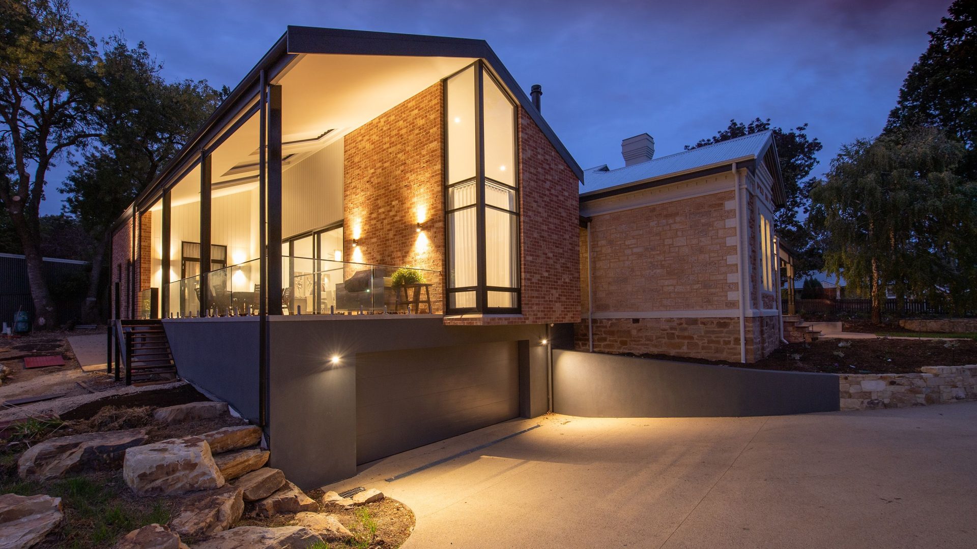 Contemporary brick-and-glass house lit at blue hour beneath a dark blue sky.