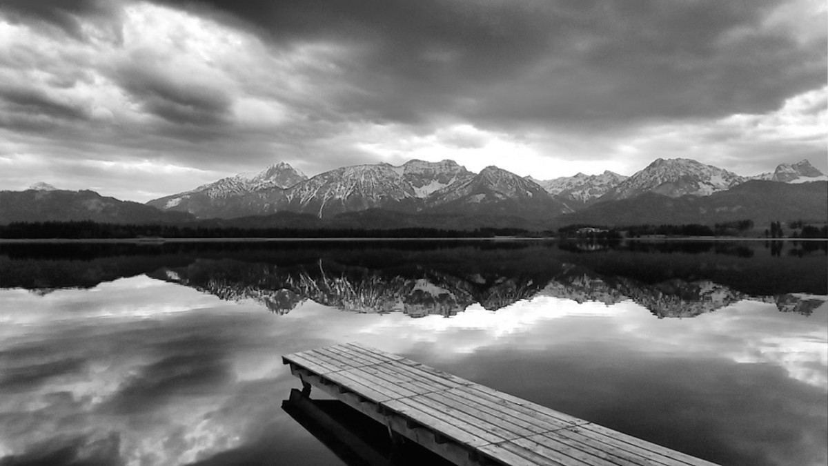 Black-and-white mountain landscape reflected in a lake, with a pier in the foreground