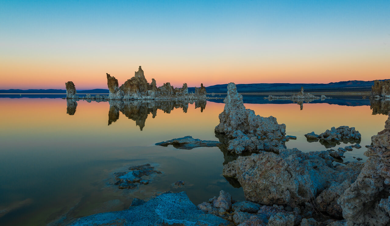 Tufa towers reflected in the still water of Mono Lake at twilight, with pale limestone in the foreground.