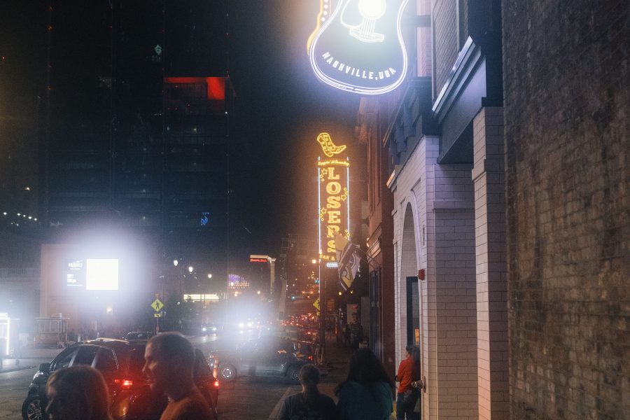 People walking along a sidewalk beneath a bright guitar sign at night