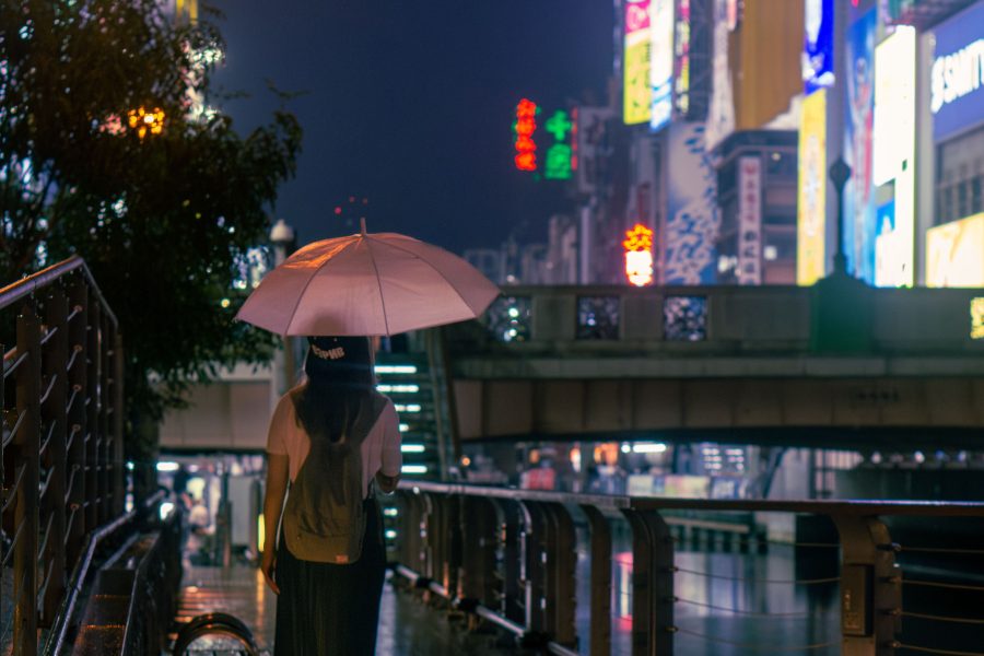 Person holding an umbrella on a rain-wet Osaka street lit by signs at night