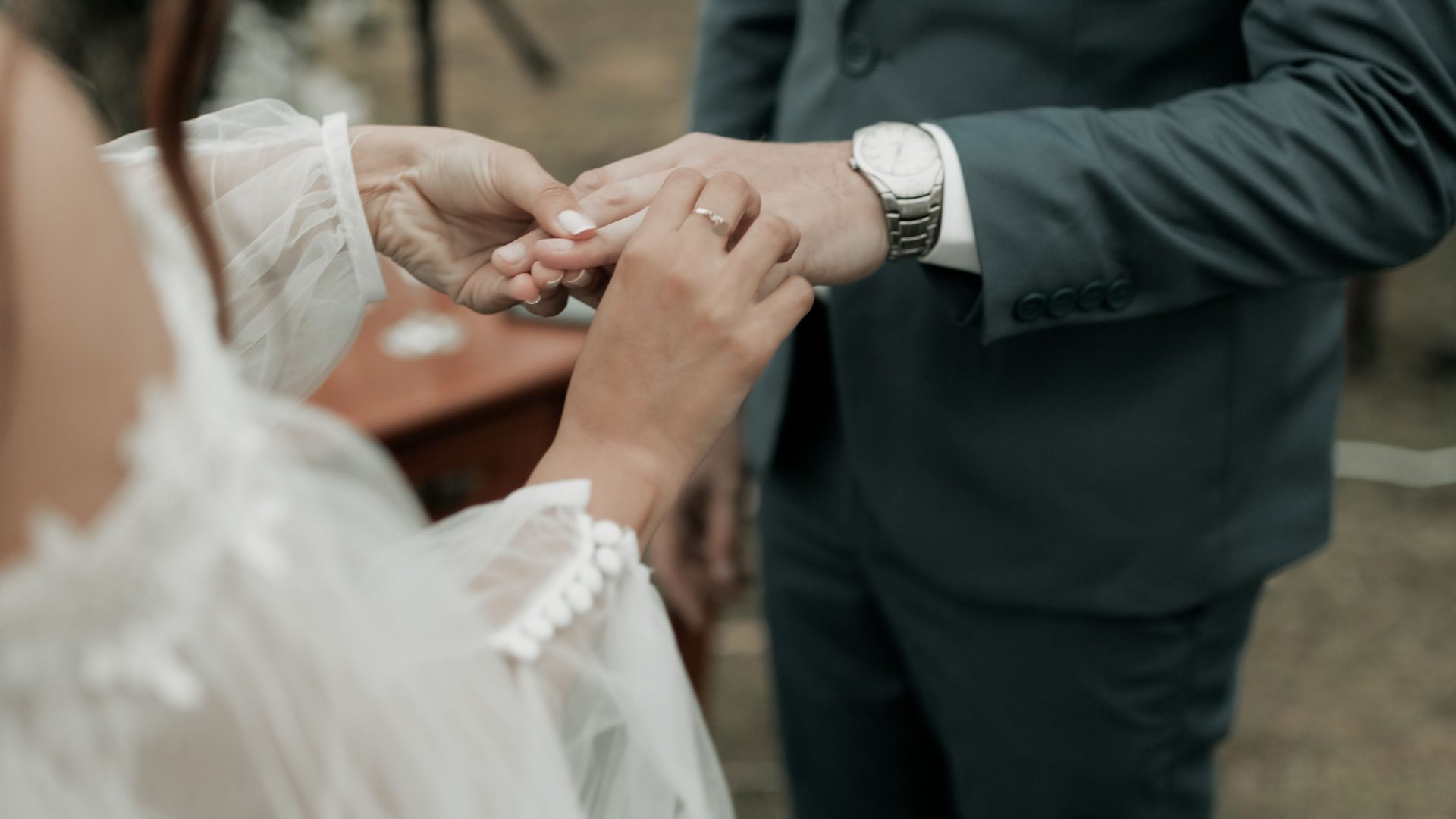 Bride placing a ring on the groom's finger during an outdoor ceremony