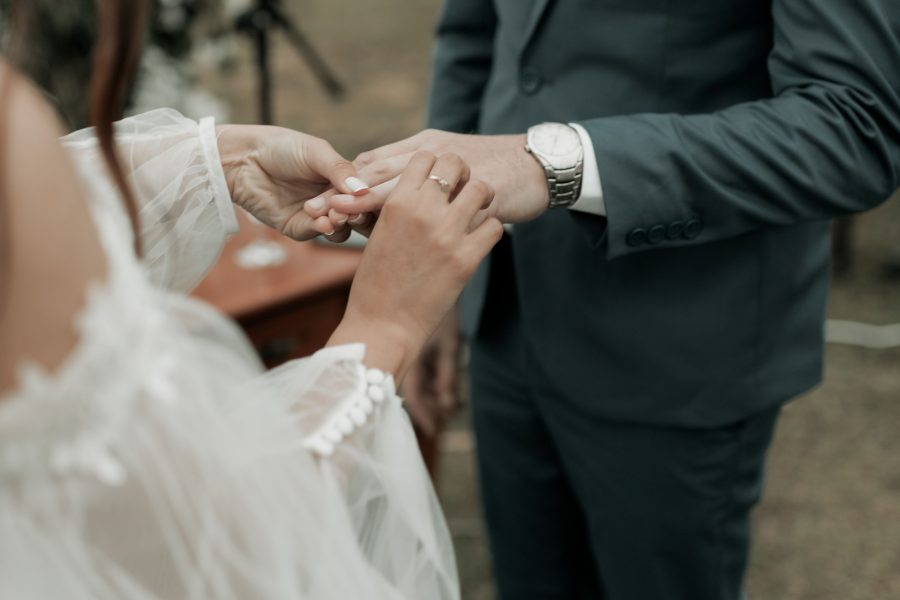 Bride placing a ring on the groom's finger during an outdoor ceremony