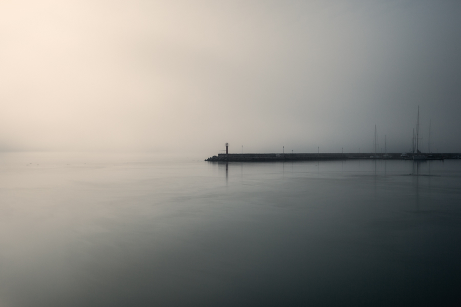 A narrow harbor breakwater and small figure in pale morning mist.