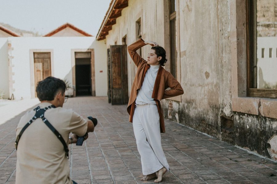 Photographer kneels with a camera facing a woman posing with one arm raised in an outdoor courtyard.