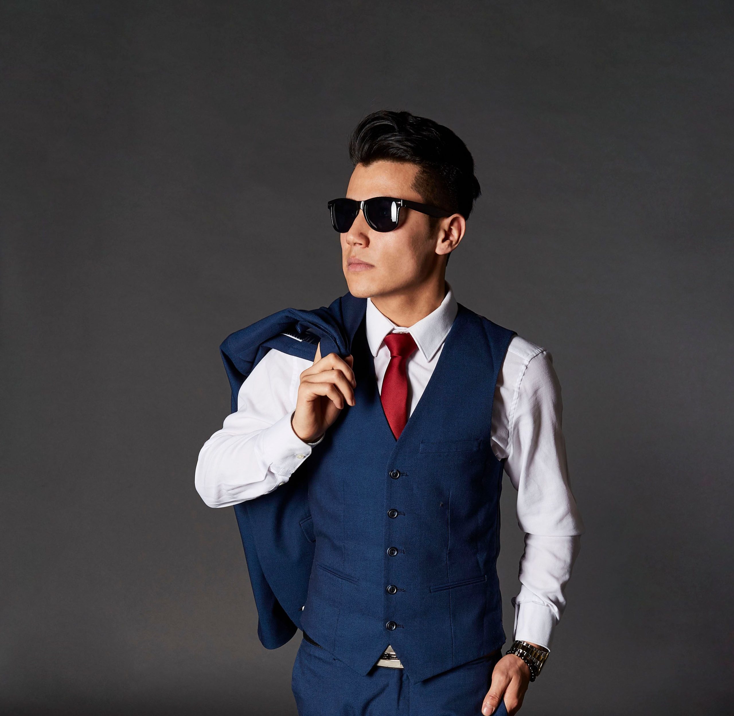 Man in a blue vest and sunglasses against an even gray background