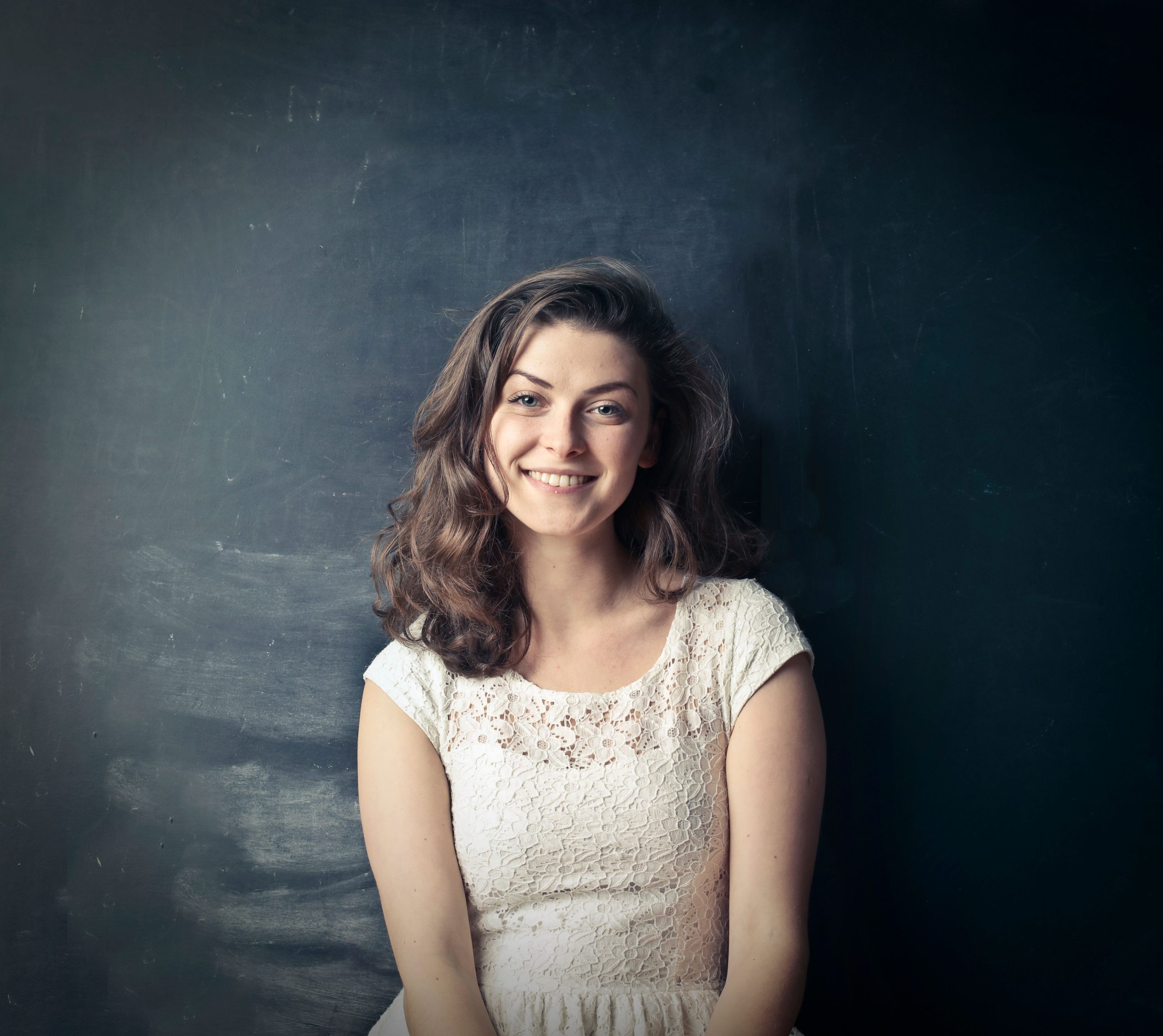 Smiling woman in a white top against a dark textured wall