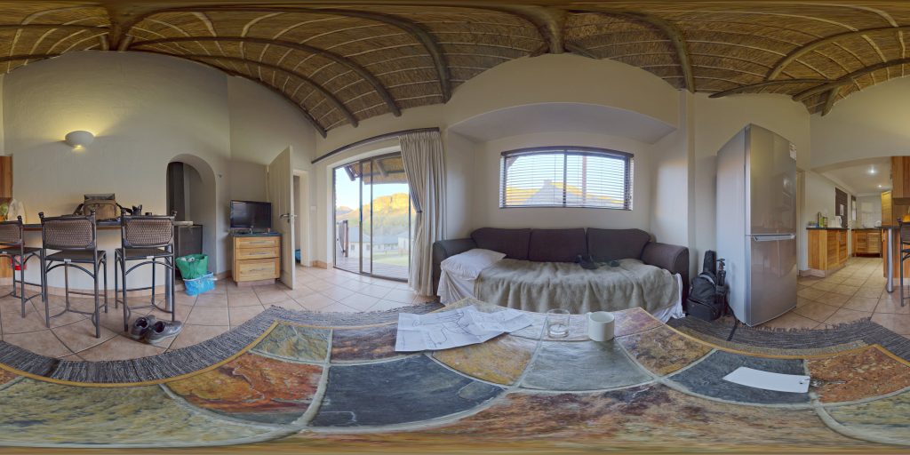 Equirectangular panorama of a lounge with a sofa, dining table, kitchen and tiled floor