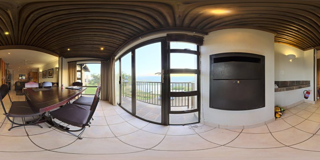 360-degree panorama of a room with lounge chairs, balcony doors and a water view