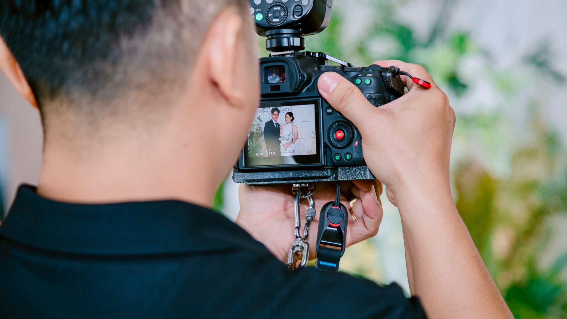 Photographer reviews a camera image of a couple at a wedding, with flash mounted above the camera