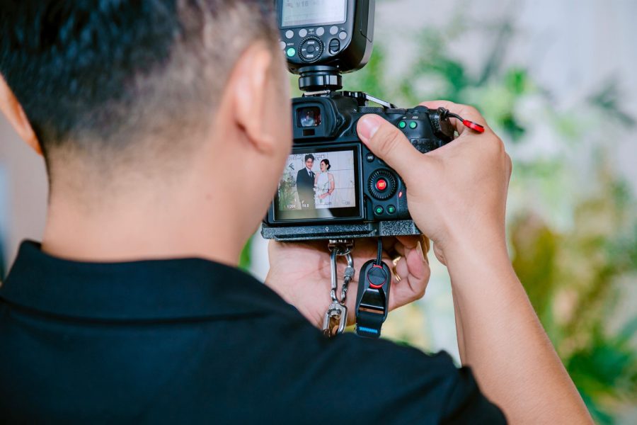 Photographer reviews a camera image of a couple at a wedding, with flash mounted above the camera
