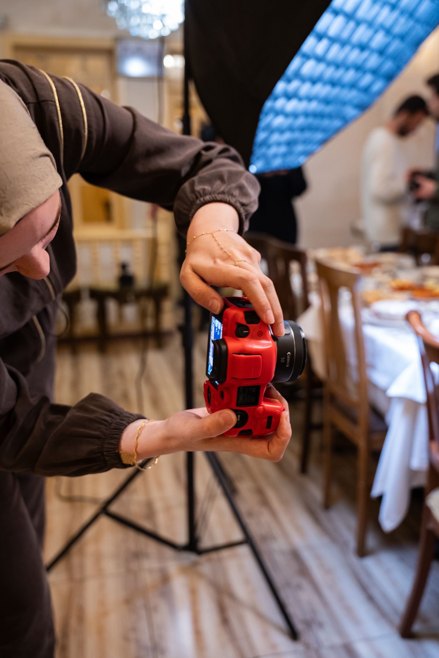 Event photographer adjusting a camera with a 50mm lens beside dressed tables at an indoor venue