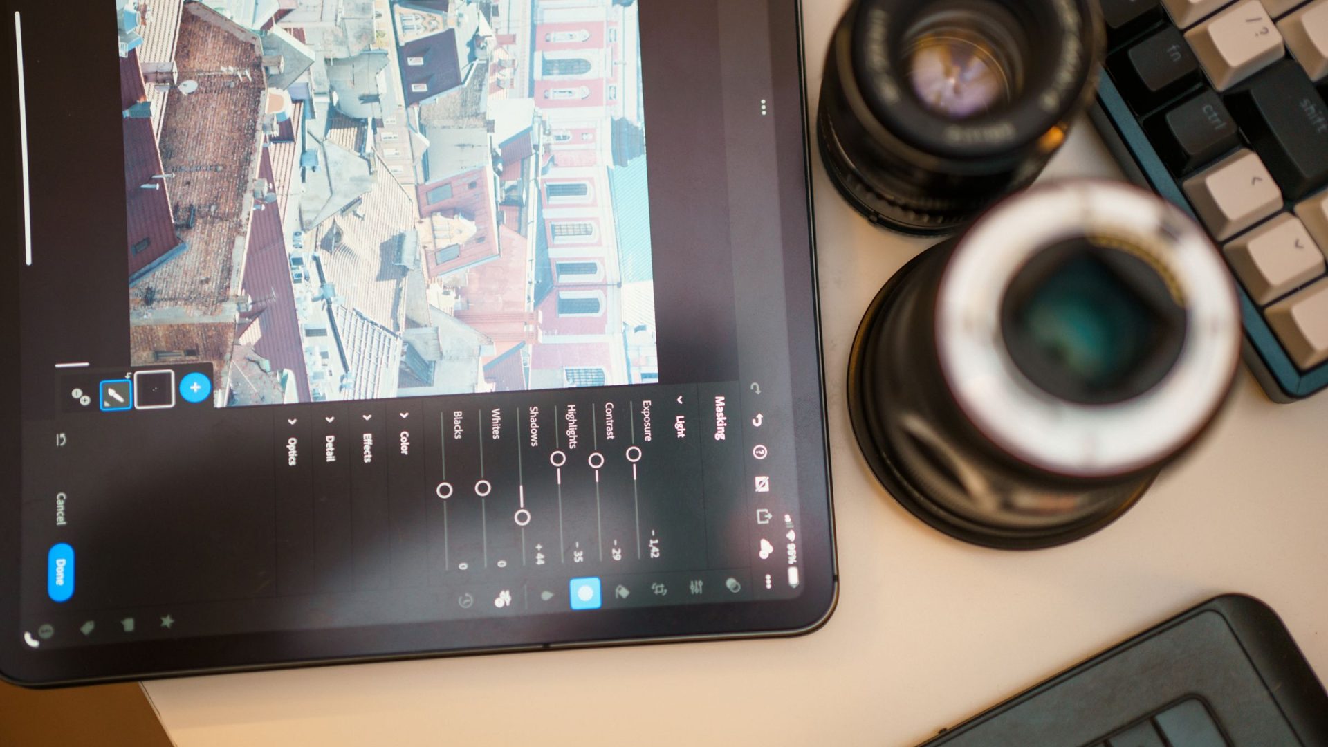 Photo editing controls on a tablet beside camera lenses and a keyboard