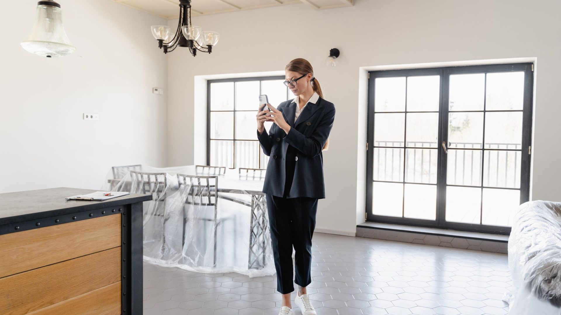 Woman photographing a bright, unfurnished home interior with a smartphone
