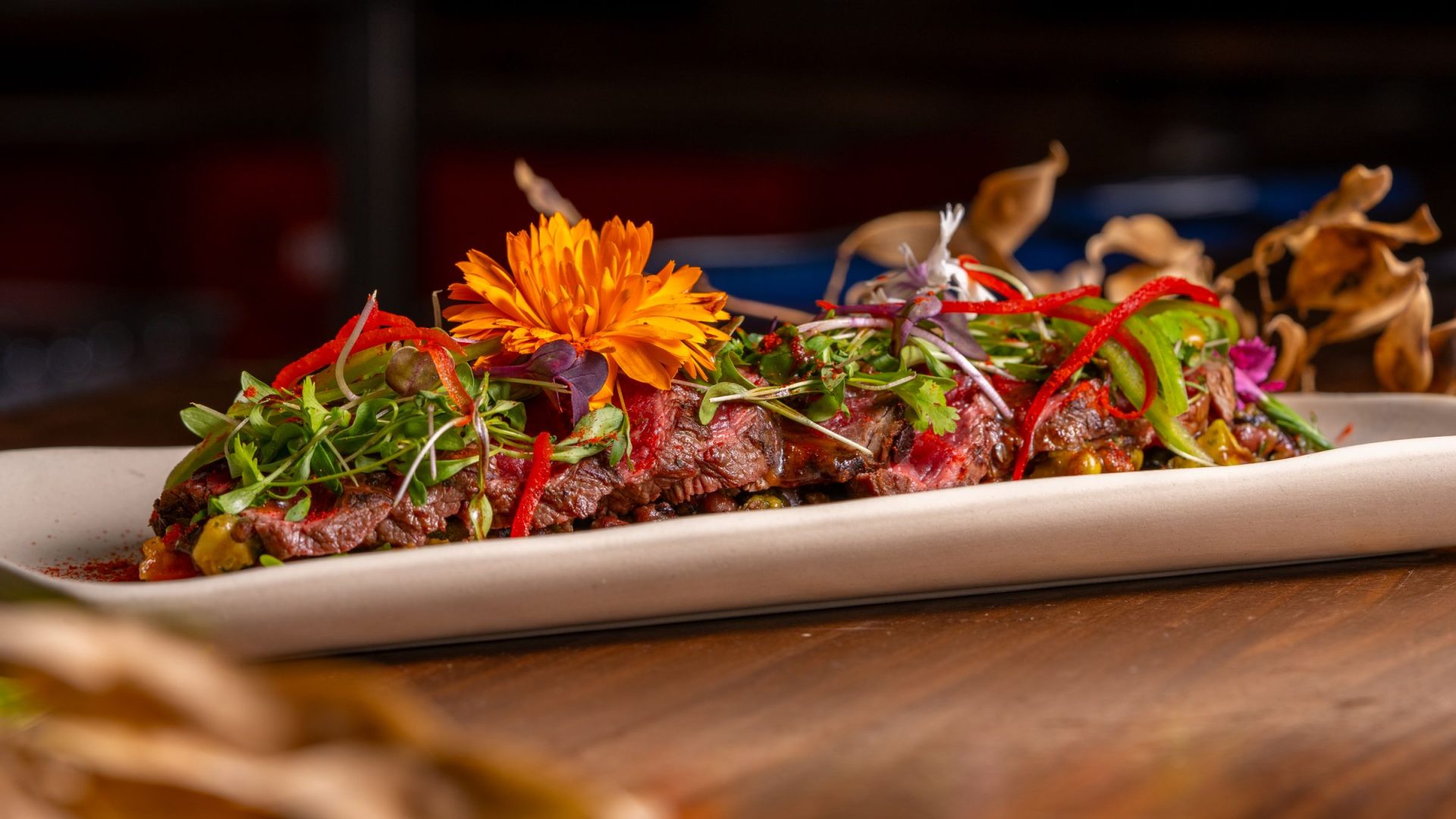 Plated meat with greens, red peppers and an orange edible flower on a restaurant table